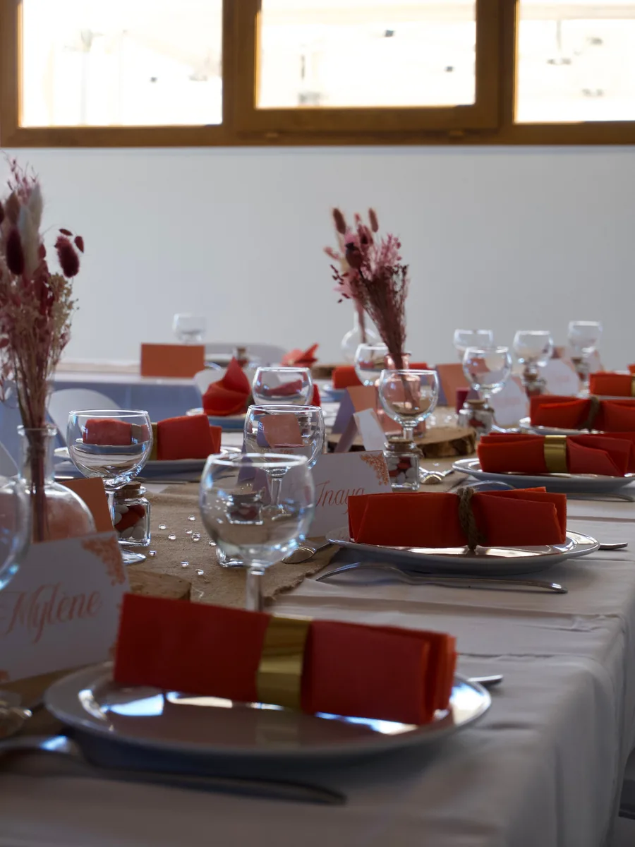 Table de fête dressée : assiettes blanches, serviettes terracotta, chemin de table en jute, bougies et marque-places avec des prénoms